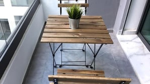 Une table en bois, accompagnée de deux bancs, sur un balcon, avec un pot de fleurs posé sur le dessus.