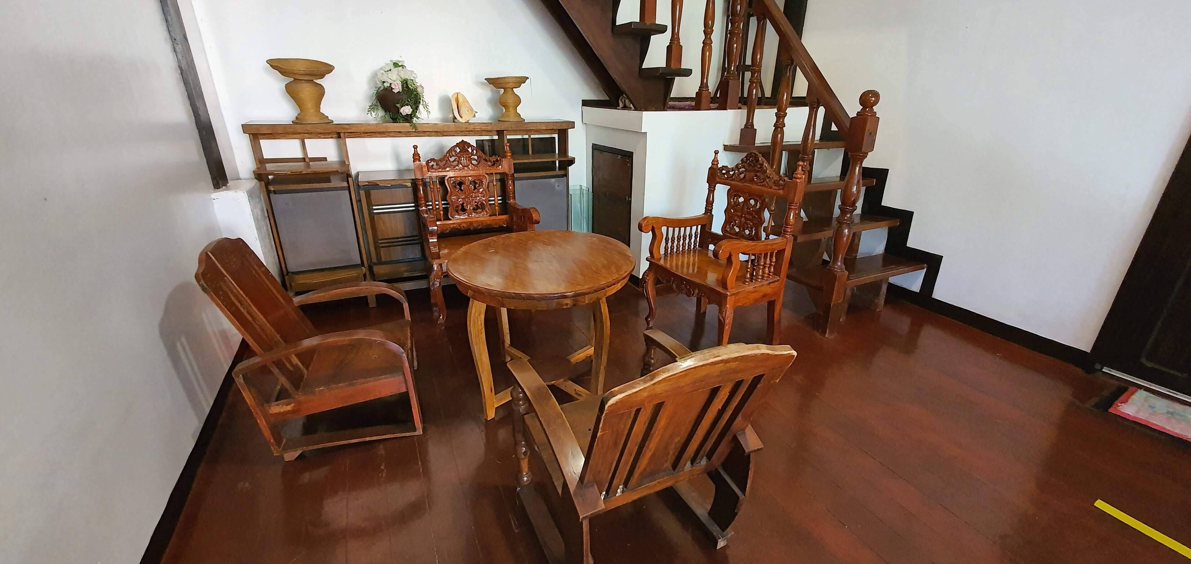 A room with a wooden dining table and chairs, a staircase, and a shelf with decorative items.