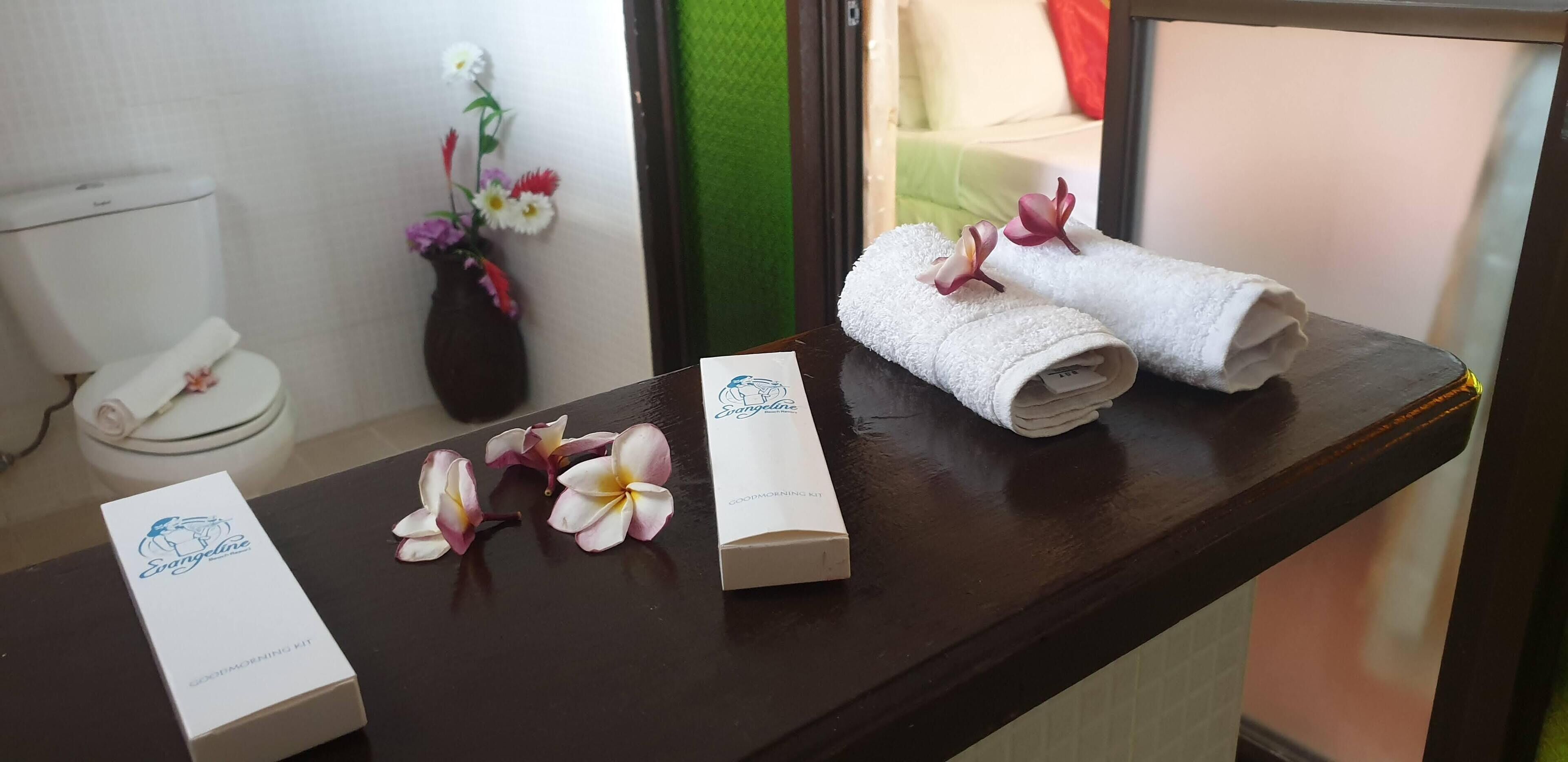 Un baño con inodoro, un florero con flores y toallas sobre una encimera.