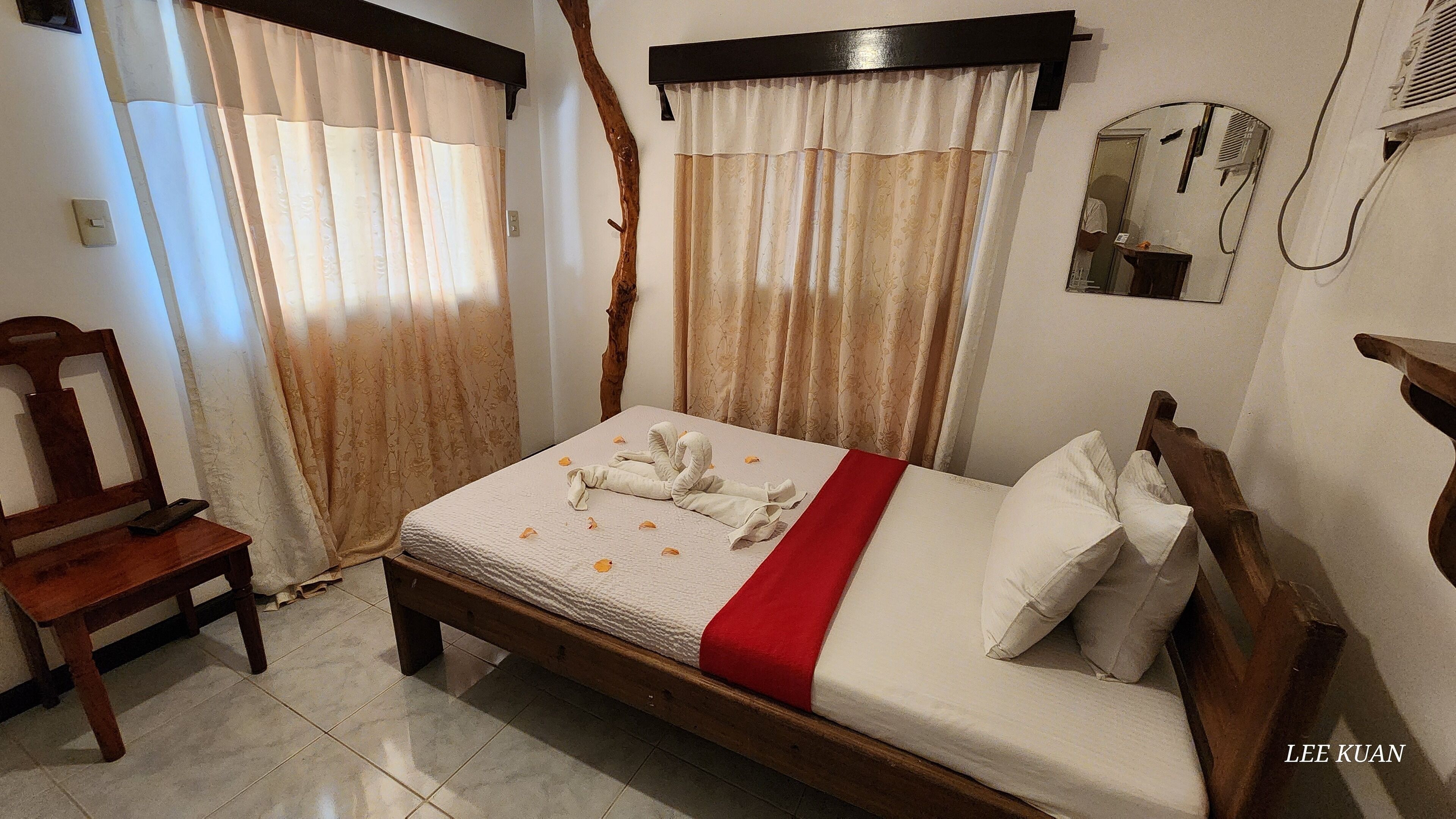 Habitación de hotel con cama y silla de madera, una mesita de noche y un espejo en la pared.