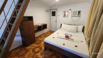 Quarto de hotel com uma cama, um guarda-roupa de madeira, uma pequena estante, uma porta e um ar condicionado fixado na parede.