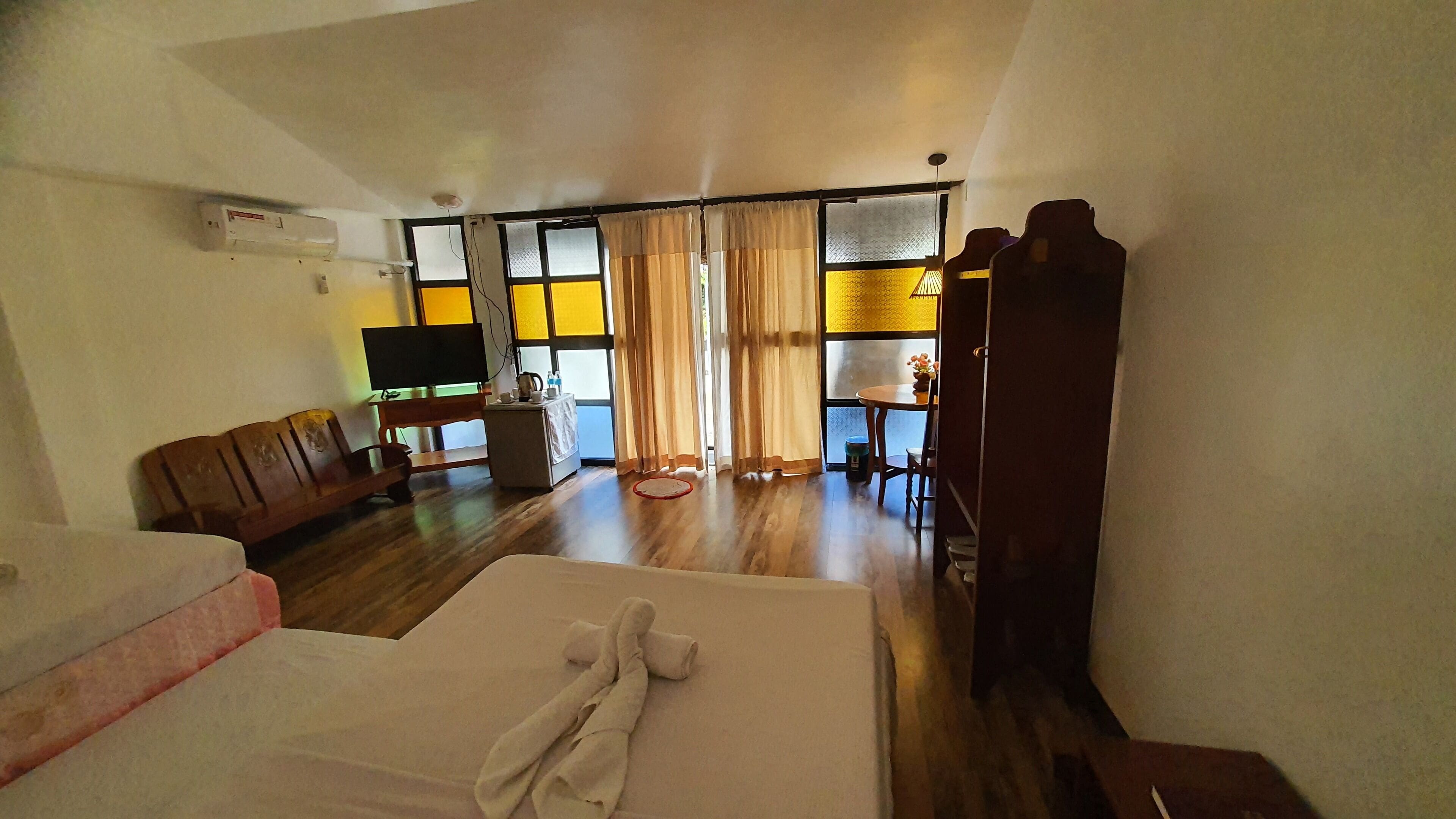Ein Hotelzimmer mit Bett, Sofa, Fernseher, einem kleinen Tisch mit Lampe und Blick durch Vorhänge.