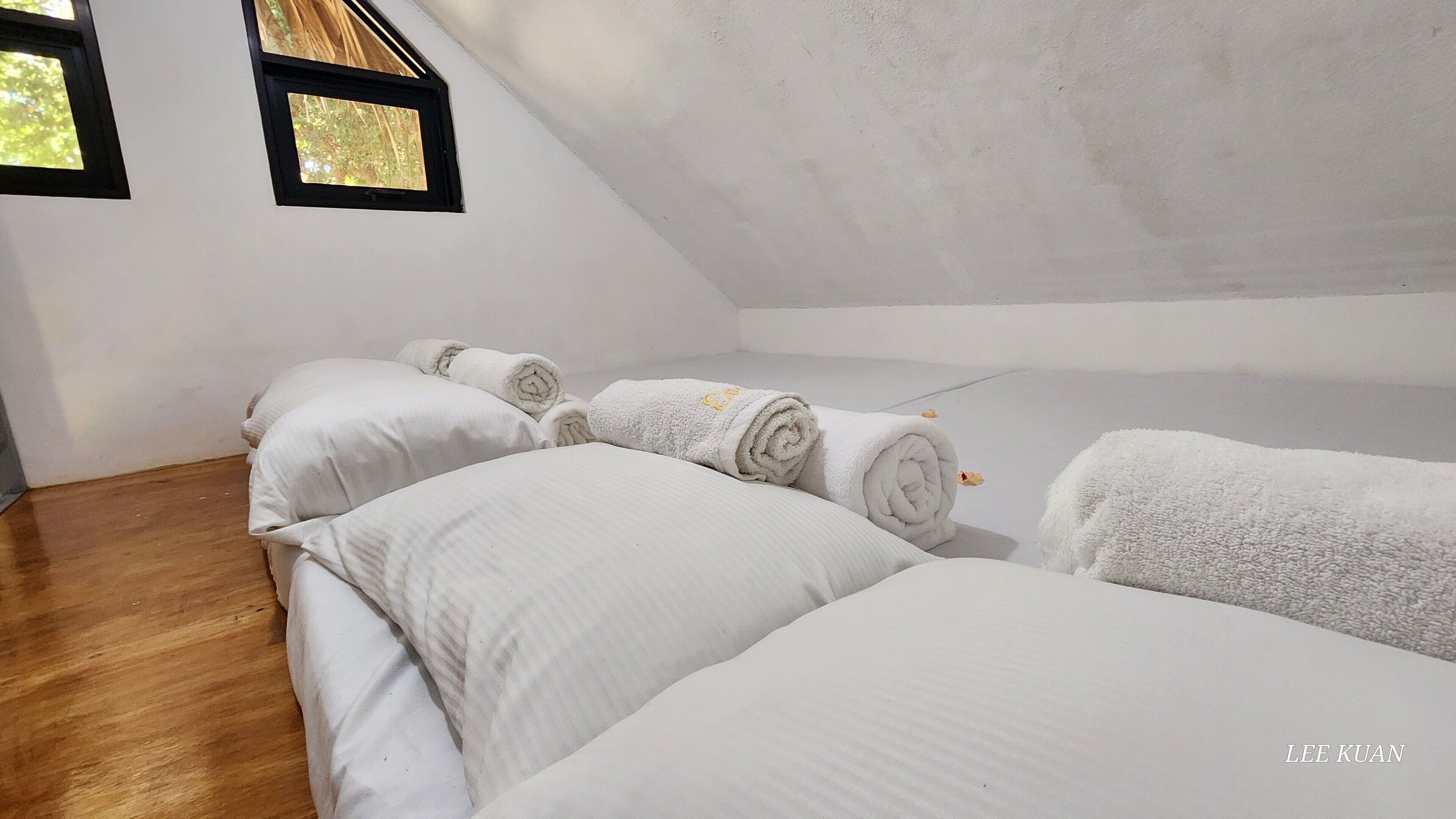 A room with a sloped ceiling, wooden flooring, and white bedding.