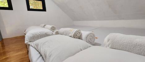 A room with a sloped ceiling, wooden flooring, and white bedding.