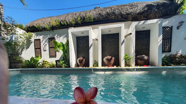 Una piscina con techo de paja, rodeada de paredes blancas y plantas tropicales.