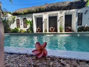 A pool with a thatched roof structure, surrounded by white walls and tropical plants. - Evangeline Beach Resort (Pagudpud)