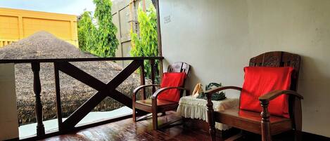 A wooden deck with two rocking chairs and a table, overlooking a garden with trees and a building in the background.