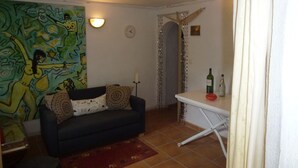 A living room with a dark blue sofa, a red rug, a white table with bottles, a wall clock, and a colorful abstract painting. - villa ground floor apartment (Dénia)