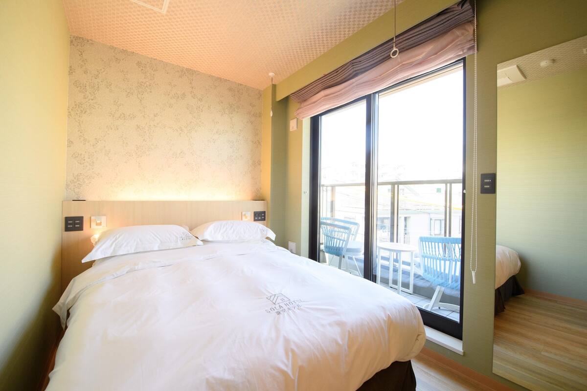 Une chambre d’hôtel avec un grand lit, une fenêtre donnant sur l’extérieur et un balcon avec des chaises.