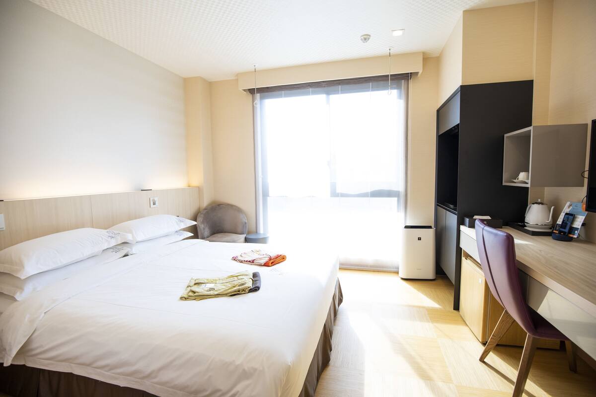 Une chambre d’hôtel avec un lit, un bureau, une chaise, une télévision et une fenêtre.