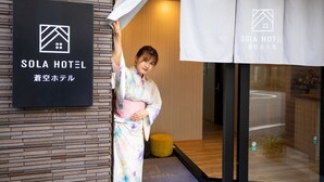 A woman in a kimono standing in front of a hotel entrance with a sign that reads "Sola Hotel".