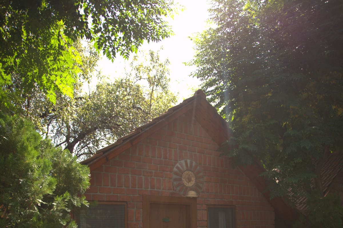 A small brick building with a wooden door, two white chairs, and a window.