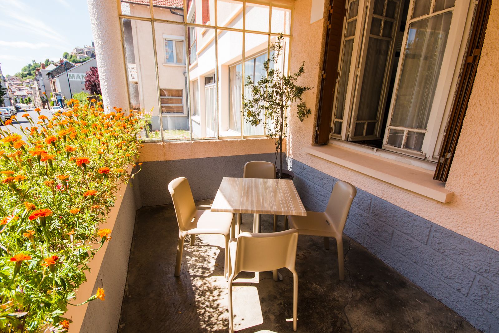 A balcony with a table and chairs, a potted plant, and a row of orange flowers.