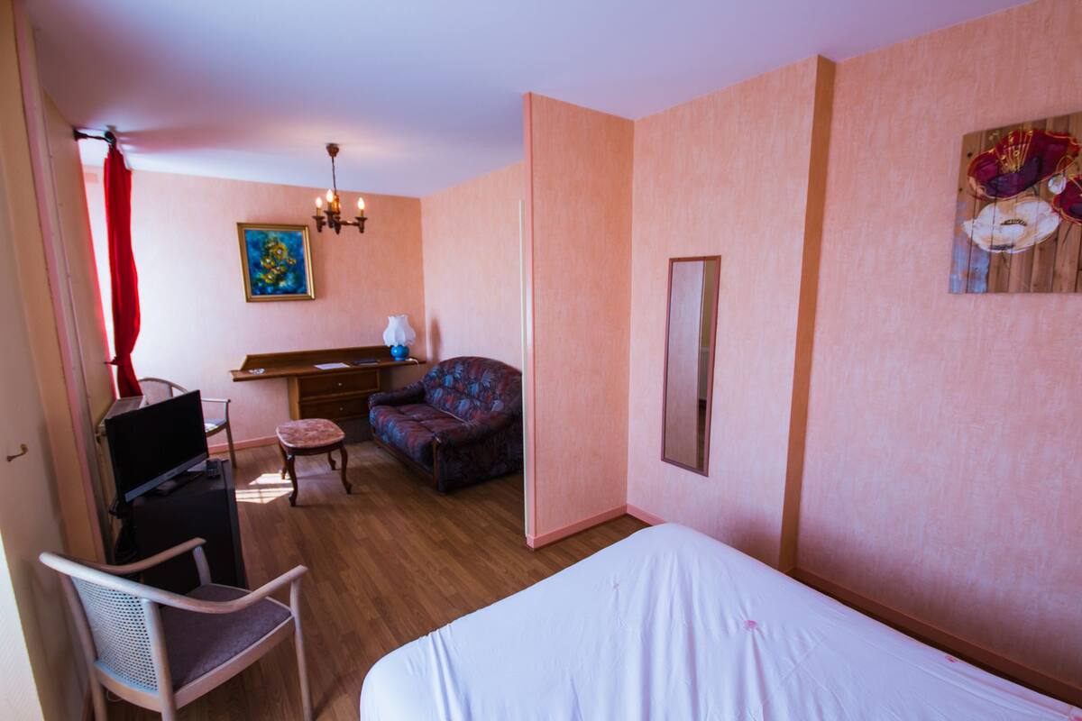 A hotel room with a bed, a desk with a chair, a sofa, a small table, and a painting on the wall.