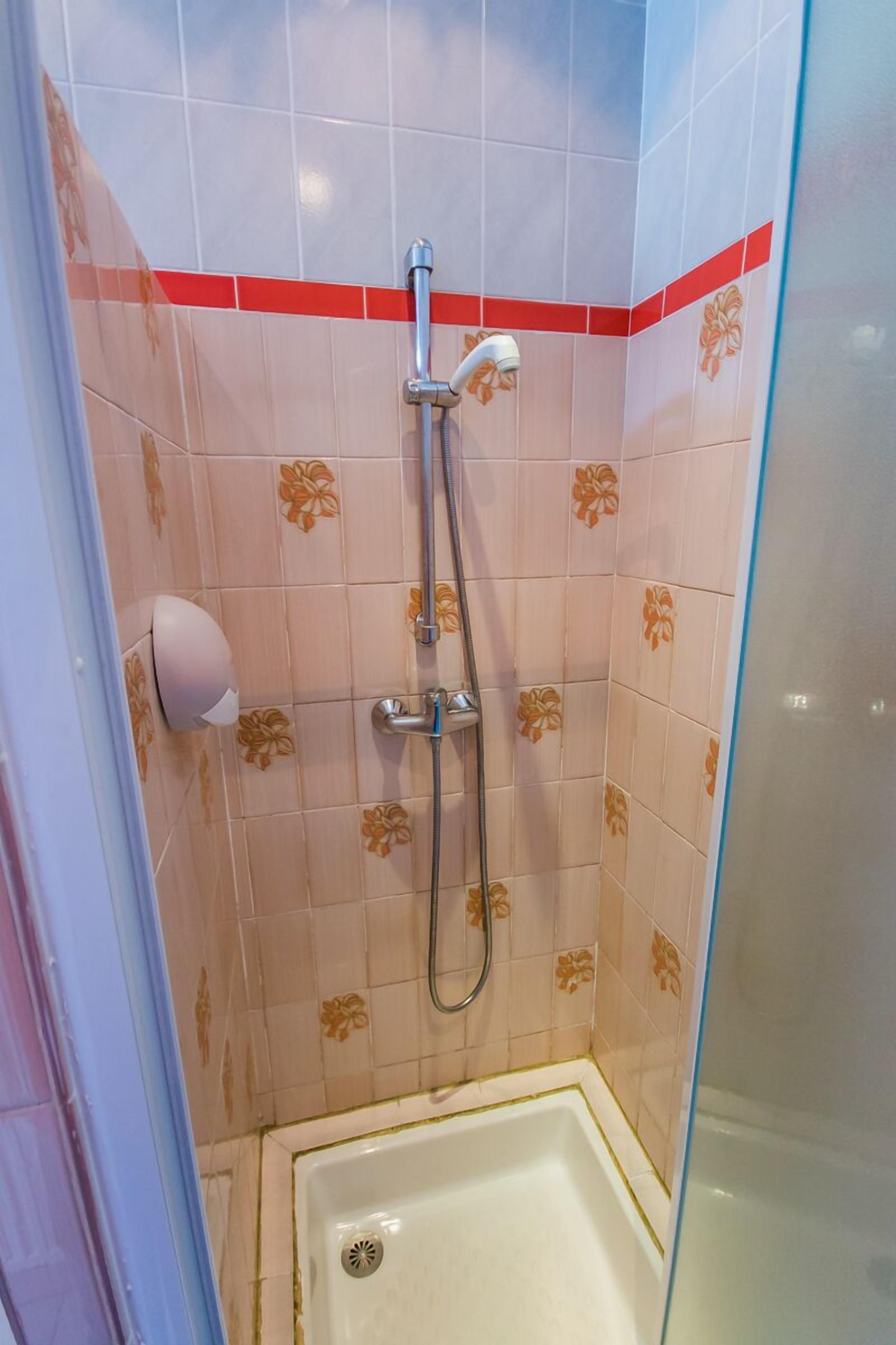 A shower area with a glass door, a handheld showerhead, a wall-mounted faucet, and a soap dispenser.