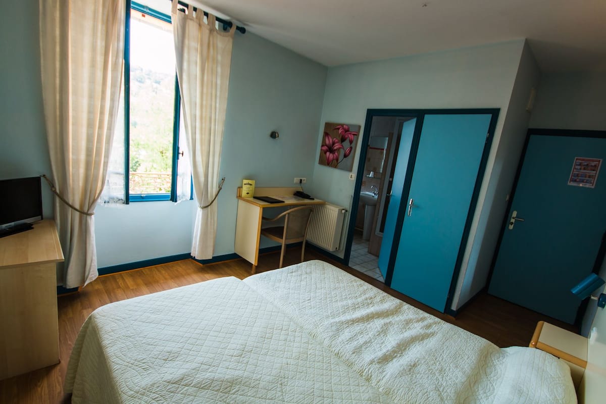 A bedroom with a bed, a desk, a chair, a radiator, and a door.