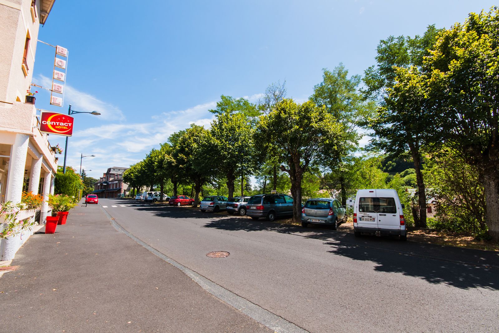 Eine Straße mit geparkten Autos und einem Hotel, an dem ein Schild mit der Aufschrift 'Kontakt Hotel' zu sehen ist.