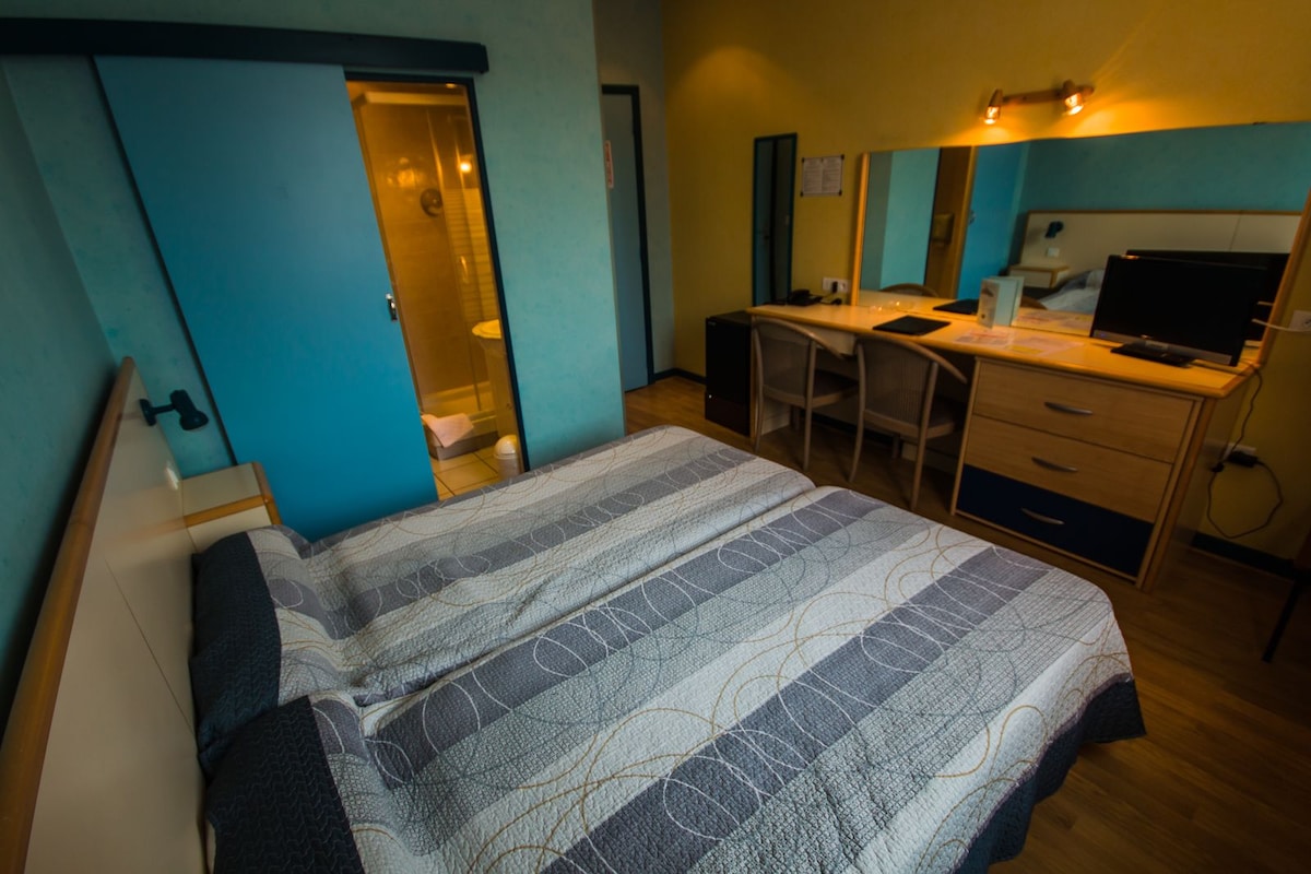 A bedroom with a bed, desk, and chair, a mirror, and a door leading to a bathroom.