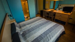 Un dormitorio con cama, escritorio y silla, un espejo y una puerta que da al baño.