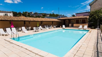 A rectangular swimming pool with a tiled deck, surrounded by white lounge chairs and tables.