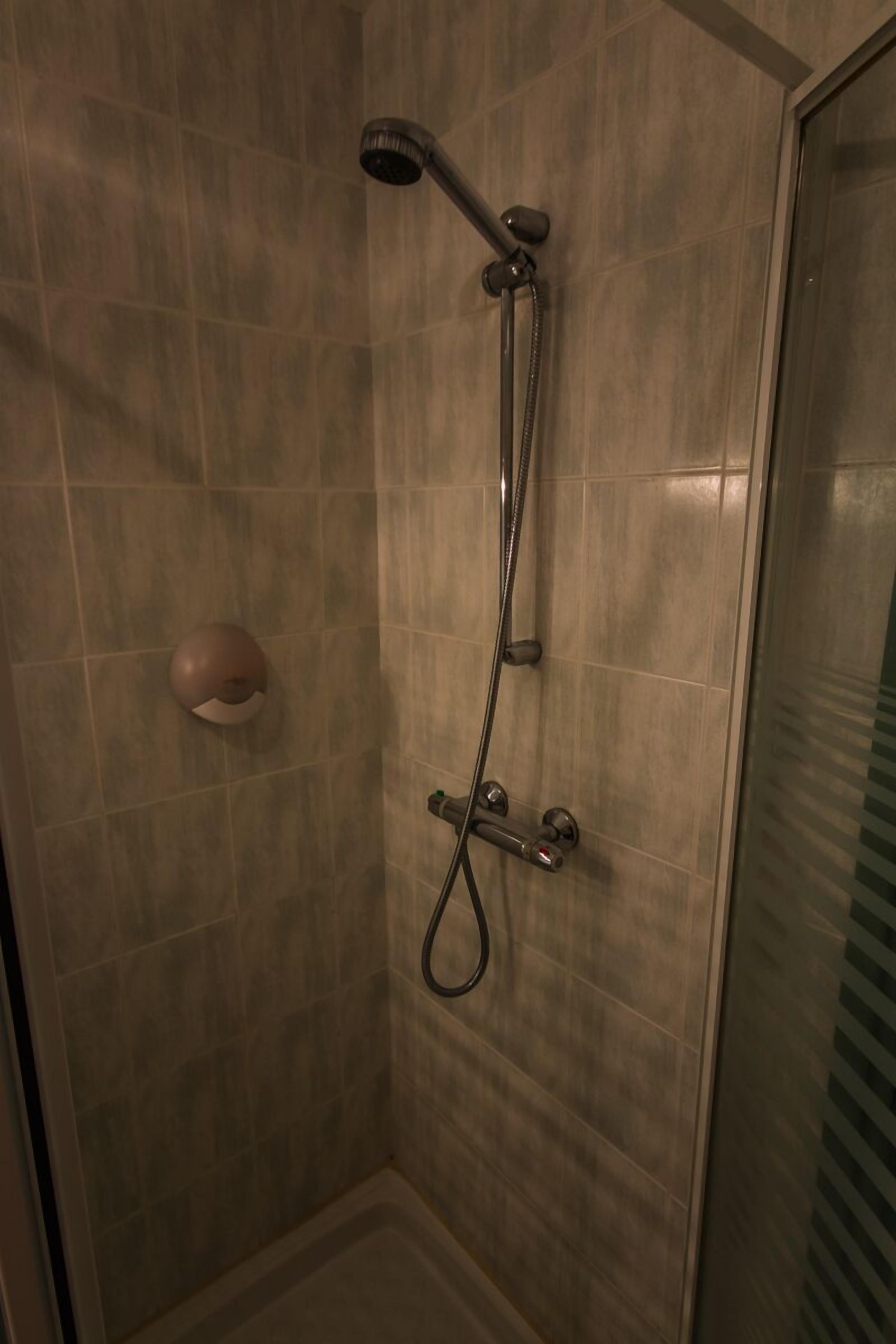 A shower with a handheld showerhead and a wall-mounted faucet.