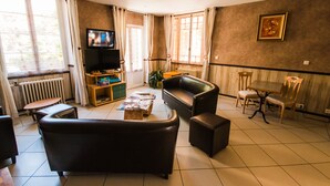 A living room with a sofa, coffee table, TV, and a dining area with chairs and a table. - Les Messageries (Saint-Flour)