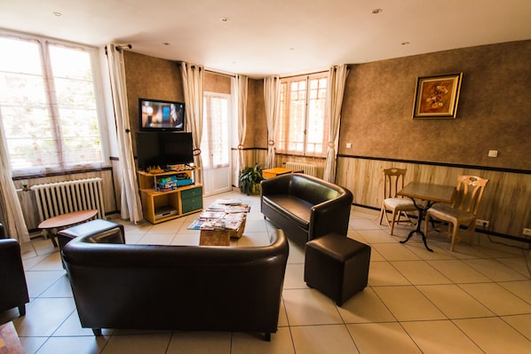 A living room with a sofa, coffee table, TV, and a dining area with chairs and a table. - Les Messageries (Saint-Flour)