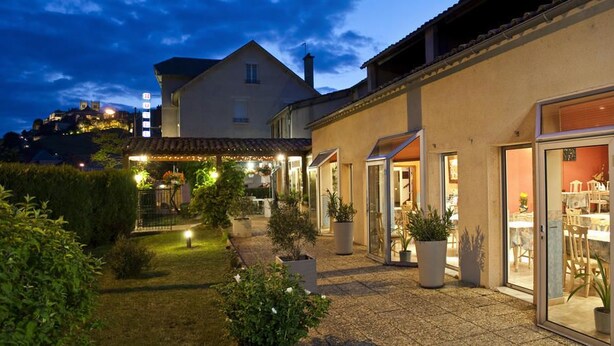 A well-lit courtyard with a covered seating area, potted plants, and a view of a hill with buildings. - Les Messageries (Saint-Flour)