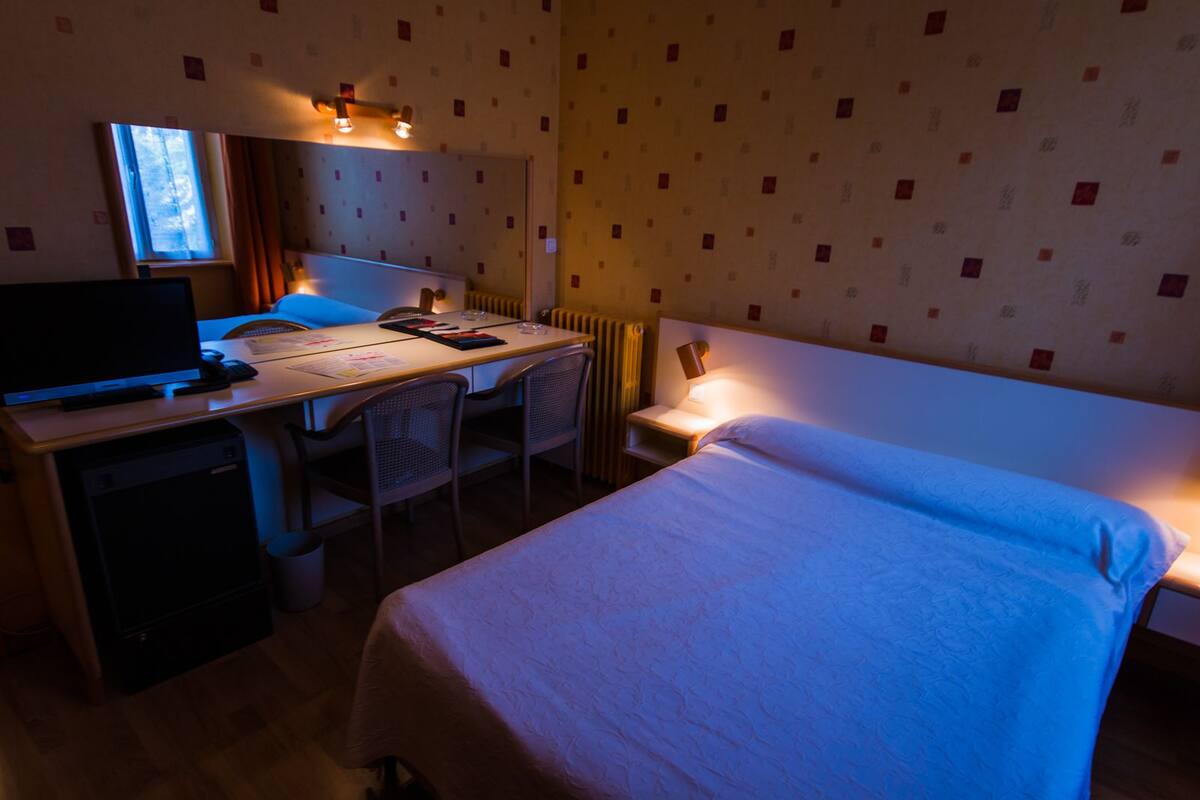 A hotel room with a bed, a desk, a chair, a TV, and a window.