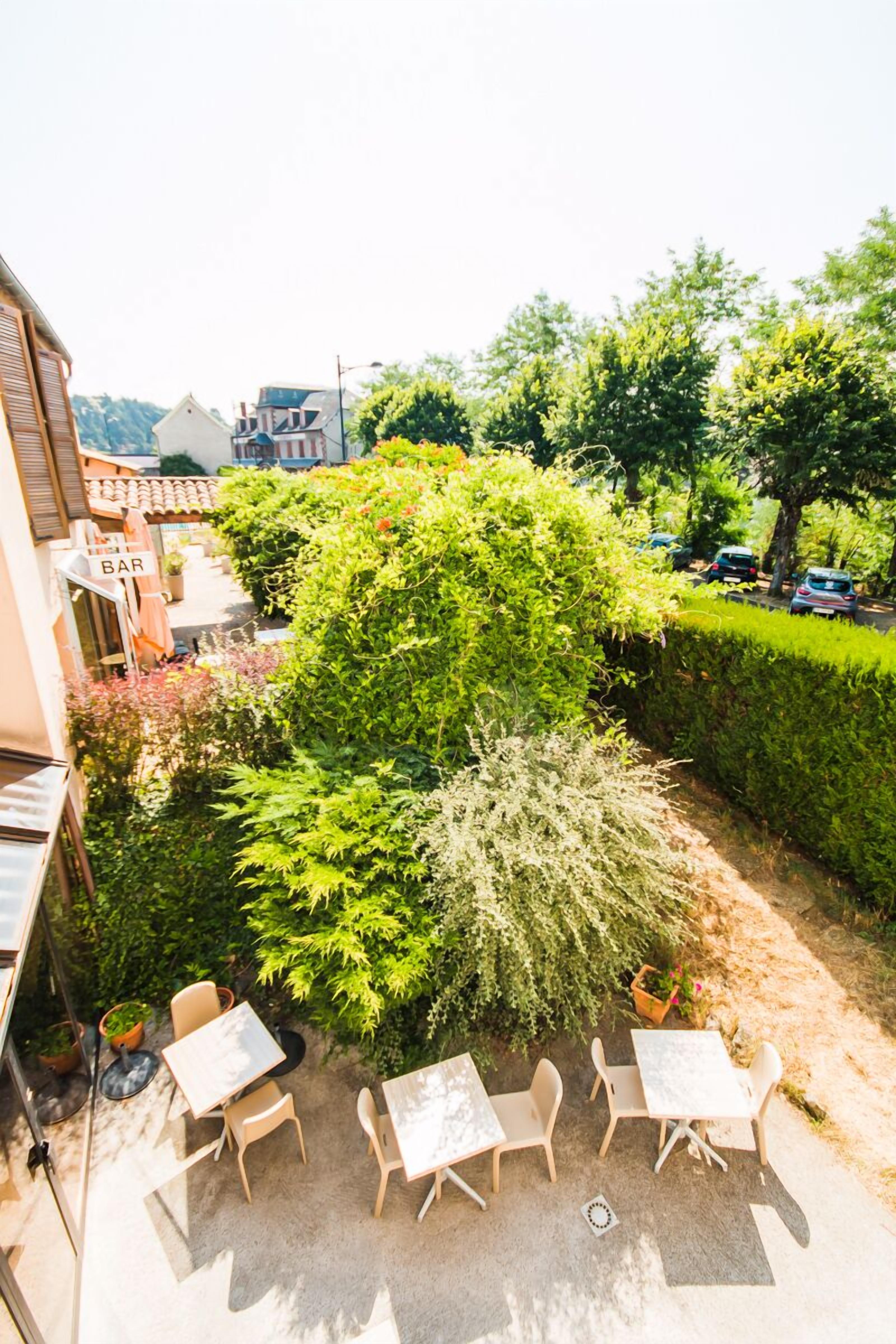Een terras met tafels en stoelen, omringd door weelderige begroeiing en een haag.
