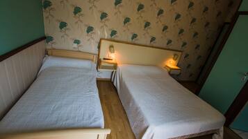 A small, cozy room with two single beds, wooden headboards, and a floral wallpaper pattern.