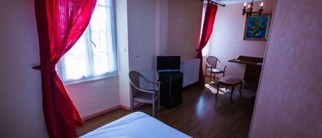 A hotel room with a bed, a desk, a chair, a television, and a painting on the wall.