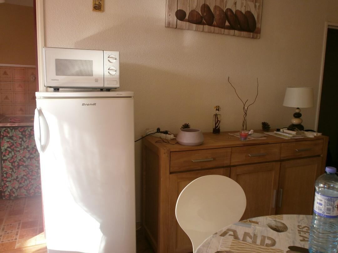 Una cocina compacta con un refrigerador blanco, un microondas encima, un armario de madera y una mesa de comedor con una silla blanca.