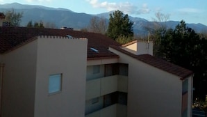 Ein Gebäude mit flachem Dach und zahlreichen Fenstern, umgeben von Bäumen und Bergen im Hintergrund.