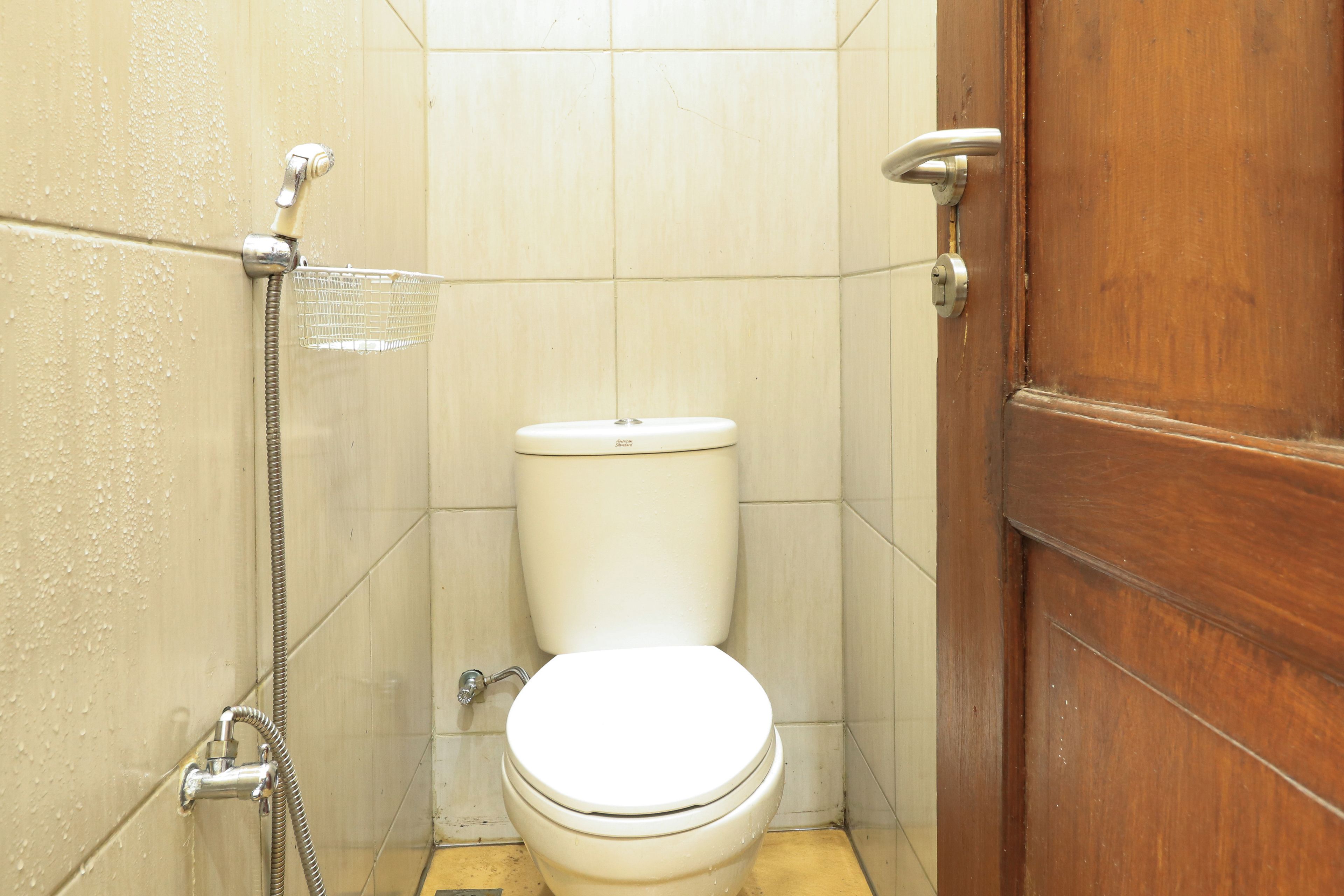 A small, compact bathroom with a toilet, a shower head, and a wooden door.