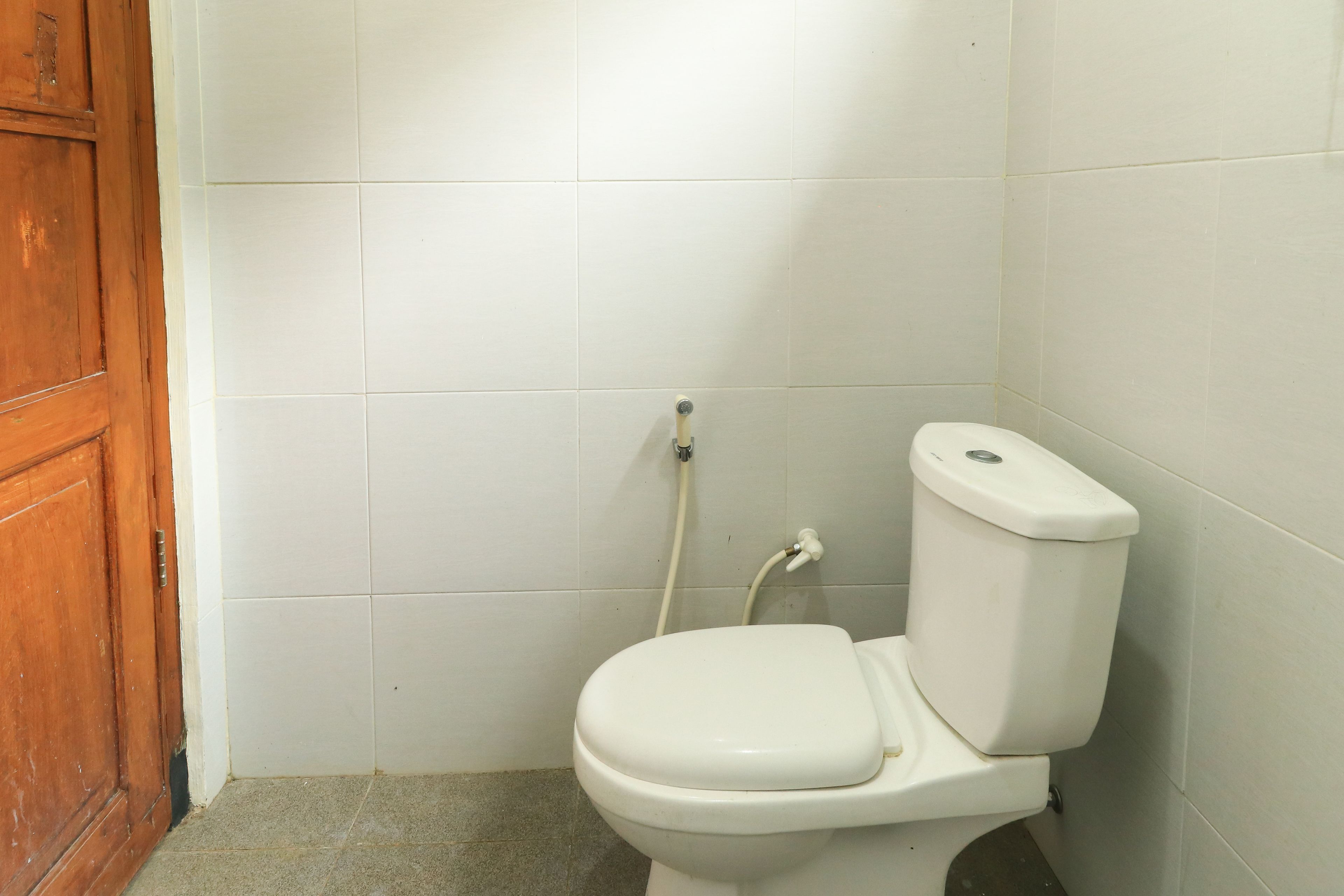 Ein kleines, sauberes Badezimmer mit Toilette, einer Holztür und weiß gefliesten Wänden.