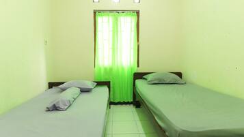 A small room with two single beds, a window with green curtains, and a light switch on the wall.