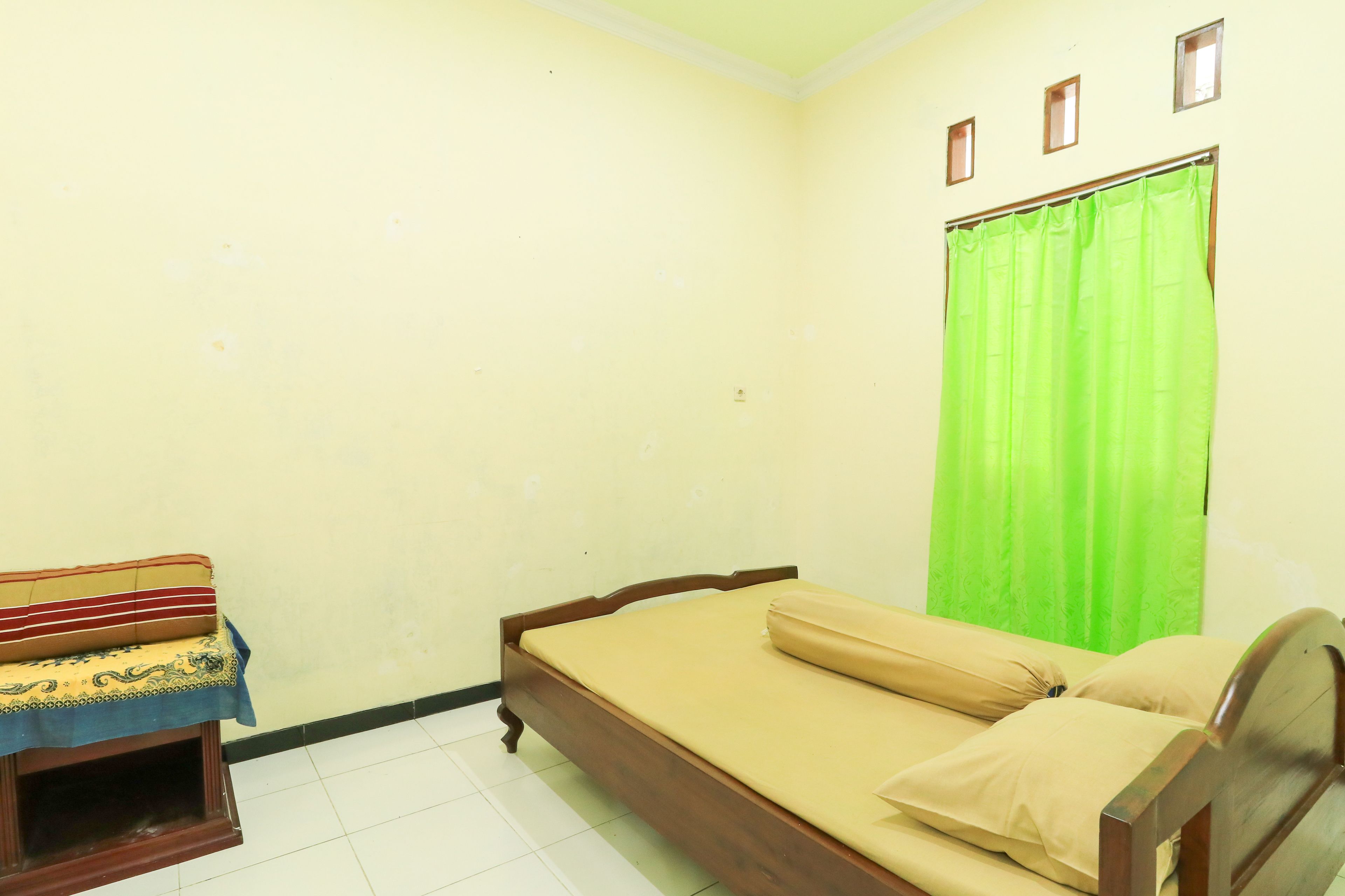 A bedroom with a single bed, a small table with a patterned cloth, and a green curtain.