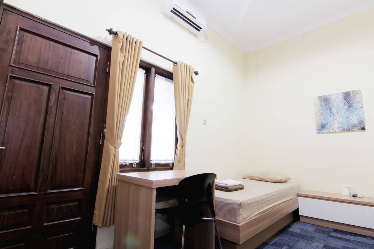 A small, compact room with a wooden desk, a black chair, a single bed, and a radiator.