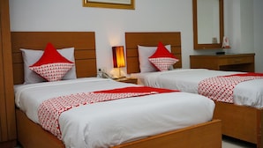 A hotel room with two beds, each with red and white bedding, a bedside table with a lamp, a wooden nightstand, and a mirror on the wall.