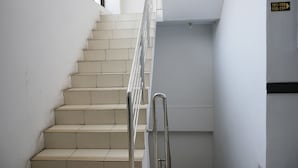 A staircase with beige steps and a metal handrail, leading to a landing with a sign indicating room numbers 101-109 and 110-116.