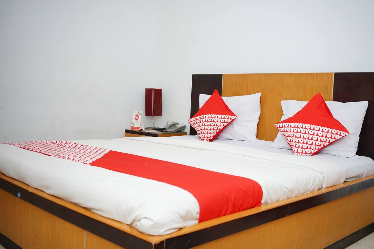 A neatly made bed with a red and white bedspread, two red pillows, and a wooden headboard.