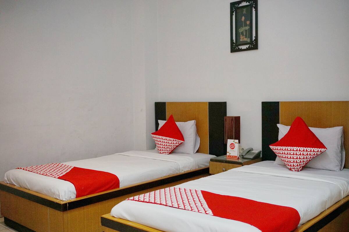 Two single beds with red and white bedding, wooden headboards, and a small bedside table with a lamp.
