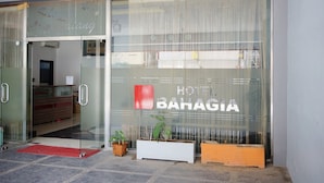 A hotel entrance with a glass door, a red mat, and potted plants outside.