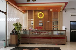 A reception desk with a wooden finish, a circular logo above it, and a sign that reads "Reception". - OYO 2291 Hotel Bahagia (Makassar)