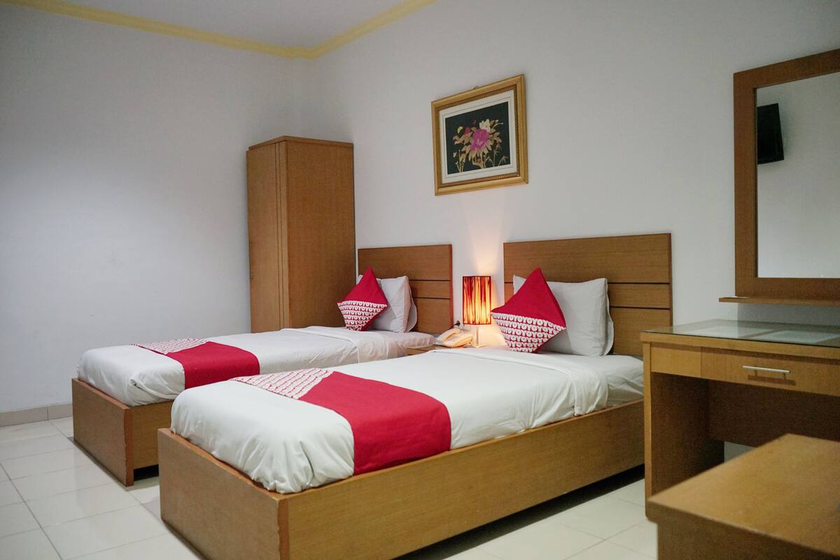 A hotel room with two single beds, a wooden wardrobe, a desk, and a mirror.