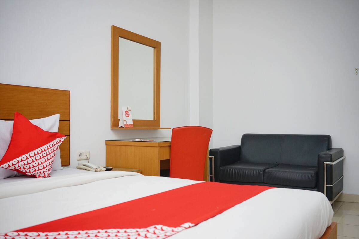 A hotel room with a bed, a desk, a chair, and a large mirror.