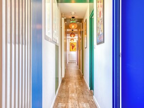 A hallway with wooden flooring, green and blue walls, and framed pictures on the walls.