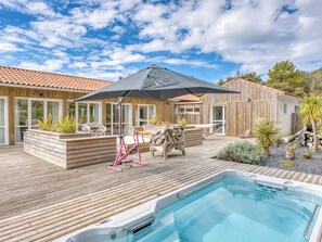 En træterrasse med et spabad, havemøbler og en stor parasol.