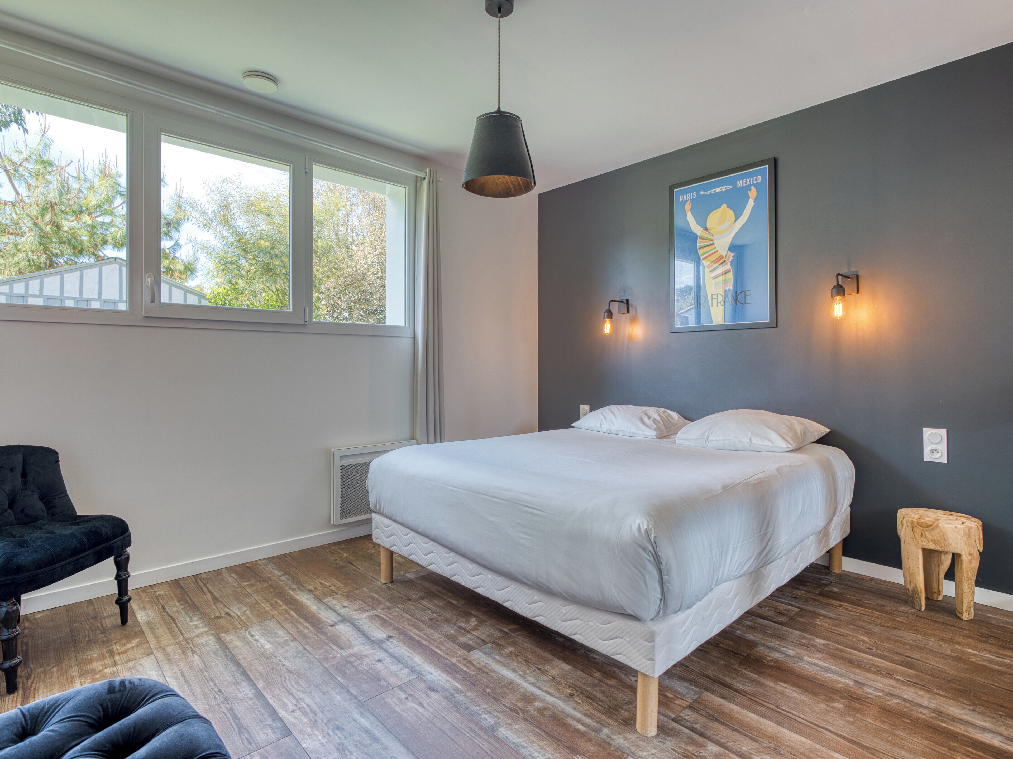 A bedroom with a large bed, a window, a chair, and a small stool.